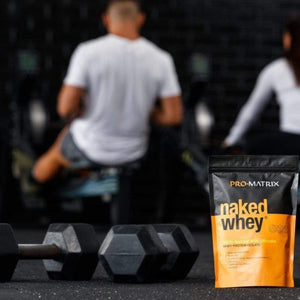 NAKED WHEY WHEY PROTEIN POWDERS 1kg UNFLAVOURED, Isolate NAKED WHEY two people in background in gym with their backs to camera on rower machine. Naked whey packet in foreground next to hand weights.