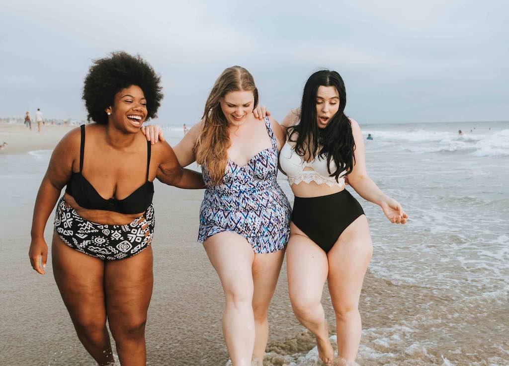 3 girls at beach laughing walking through water and sand