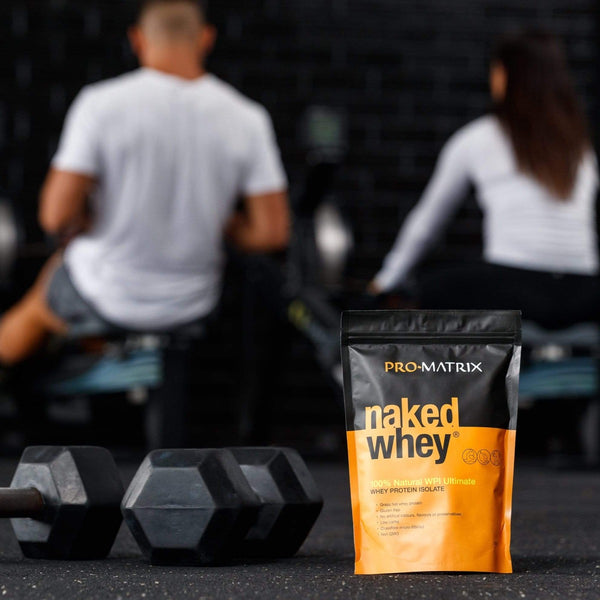 NAKED WHEY WHEY PROTEIN POWDERS 1kg UNFLAVOURED, Concentrate NAKED WHEY. Male and Female blurred out in background at gym on rowwers with their backs to camera. naked whey packet in foreground with two sets of hand weights