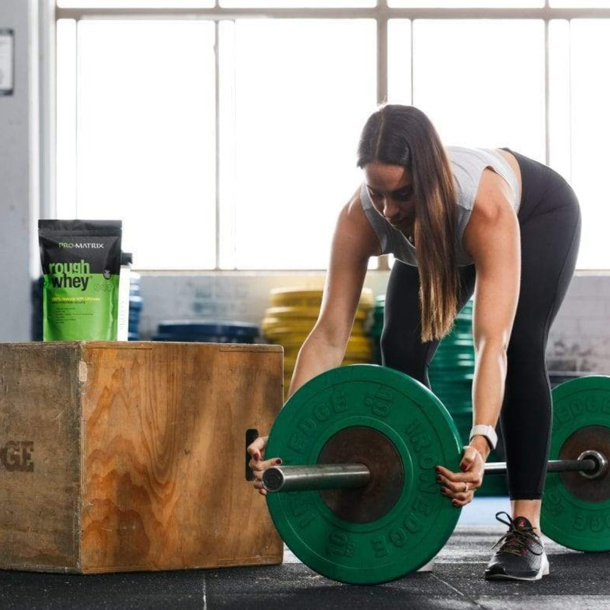 ROUGH WHEY WHEY PROTEIN POWDERS 1kg CHOCOLATE &amp; COCONUT, Concentrate ROUGH WHEY Girl changing weights on bar in gym with rough whey packet sitting on jump box