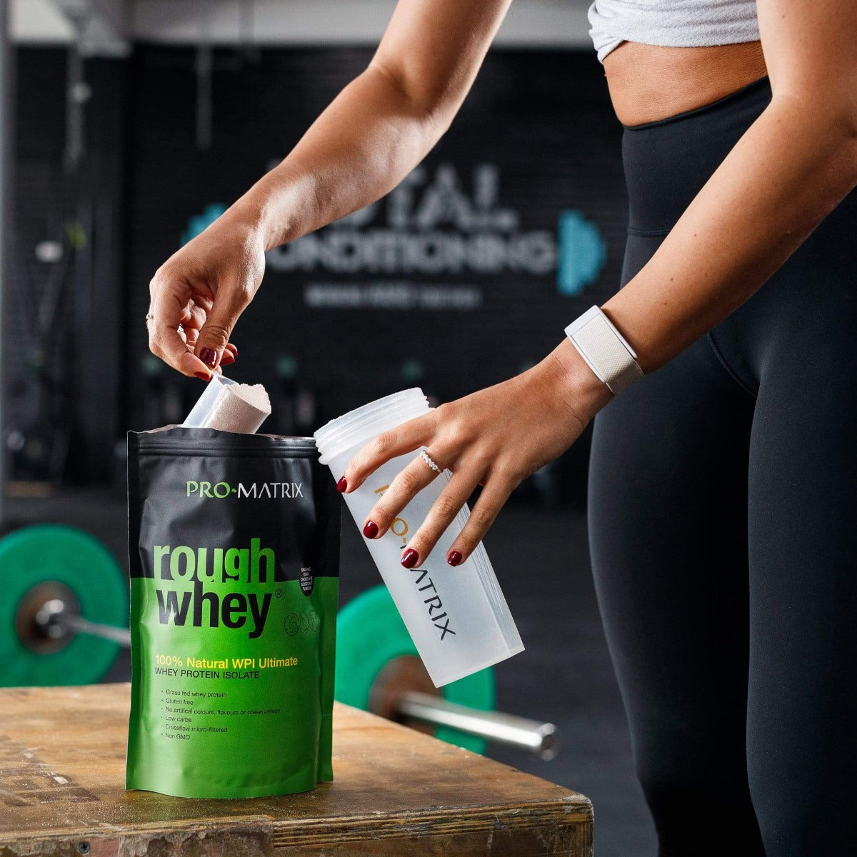 ROUGH WHEY WHEY PROTEIN POWDERS 2kg CHOCOLATE &amp; COCONUT, Isolate ROUGH WHEY. Person in gym clothes inside gym scooping powder from rough whey packet in to pro matrix shaker. gym bar and weights in background