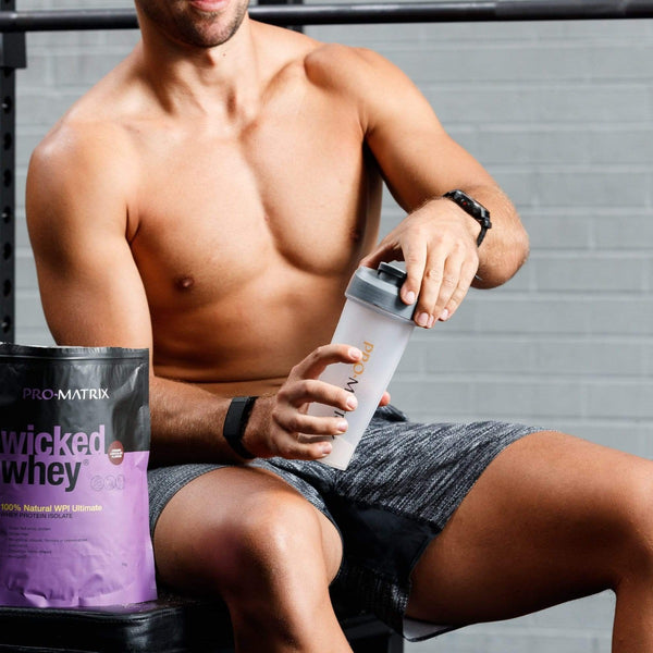 WICKED WHEY WHEY PROTEIN POWDERS 2kg CHOCOLATE, Concentrate WICKED WHEY. Man in gym with shirt off holding pro matrix shaker bottle . wicked whey packet sitting on chair in foreground